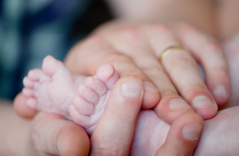 man holds the feet of a newborn baby in his hands